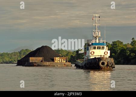 Una chiatta di carbone è trainata da un rimorchiatore sul fiume Segah a Berau, Kalimantan orientale, Indonesia. Il paese potrebbe non essere in grado di soddisfare la crescente domanda di carbone da parte dei paesi europei che stanno cercando di fare scorte di combustibile sporco, poiché riducono le importazioni di energia dalla Russia, Jakarta Post ha riferito il 1 luglio 2022. Foto Stock