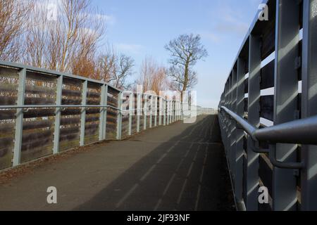 shared-use path up to a bridge over with winter trees and a blue sky with white clouds Foto Stock