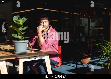 Un giovane uomo d'affari caucasico attento seduto alla scrivania in un ufficio creativo Foto Stock