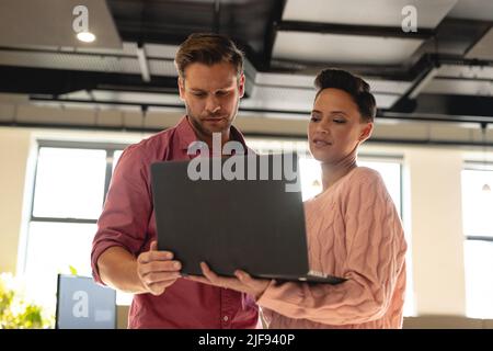 Giovane uomo d'affari e donna d'affari multirazziale che discute su laptop in ufficio creativo Foto Stock