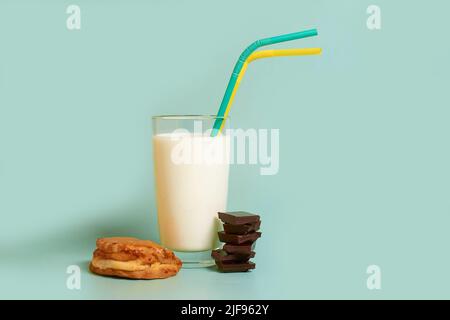 Un bicchiere di latte, due tubi di plastica, una torta e pezzi di cioccolato fondente Foto Stock