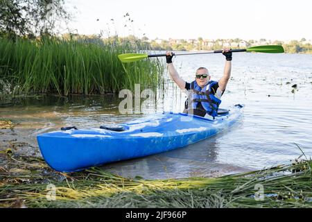 Kayak sul fiume. L'uomo caucasico adulto è seduto in un kayak e saluti. Il concetto di attività acquatiche. Foto Stock