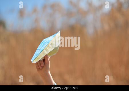 Mano che tiene la bandiera di carta dipinta nei colori della bandiera Ucraina giallo-blu. Sostenere l'Ucraina nella guerra con la Russia. papercut patriottico. Foto Stock