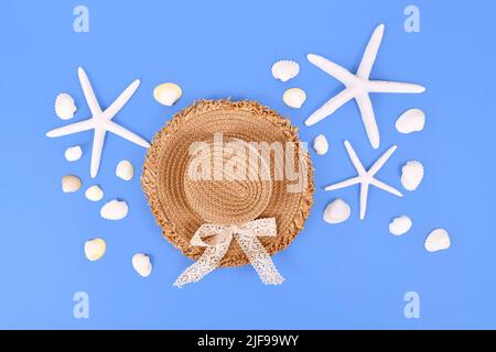 Stelle marine bianche, conchiglie e cappello estivo con paglia su sfondo blu Foto Stock