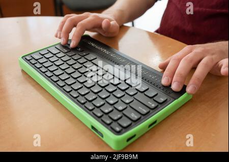 Un uomo cieco utilizza un computer con un display Braille e una tastiera per computer. Dispositivo incluso. Foto Stock