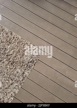 Moquette Shaggy su pavimento di legno marrone. Texture miste all'interno. Soffice tappeto sulla terrazza all'aperto coperta di terrazze. Giocattolo per bambini adagiato sul tappeto. Foto Stock