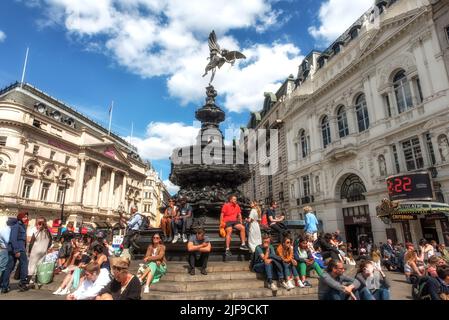 Londra, Regno Unito, Giugno 28th 2022 turisti seduti sui gradini della Shaftesbury Memorial Fountain e la statua del dio greco Anteros, Piccadilly Foto Stock