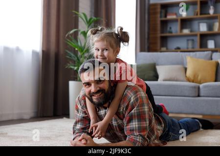 Buon ritratto di famiglia a casa. Giovane bel padre con figlia carina adagiata su un tappeto vicino al divano. Ragazza carina che abbraccia il suo caro papà Foto Stock