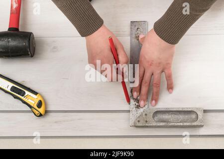 Il maestro femminile disegna una linea a matita sulla tavola, installando pavimenti in vinile al quarzo, lavori di installazione. Foto Stock