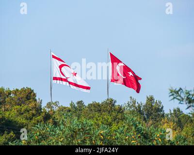 Grandi bandiere turche e nord-cipriote volano fianco a fianco in un pomeriggio soleggiato vicino a Girne, TRNC Foto Stock
