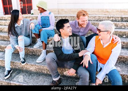Gruppo di amici che si godono il fine settimana seduti all'aperto. Persone multietniche che parlano a scale. Foto Stock
