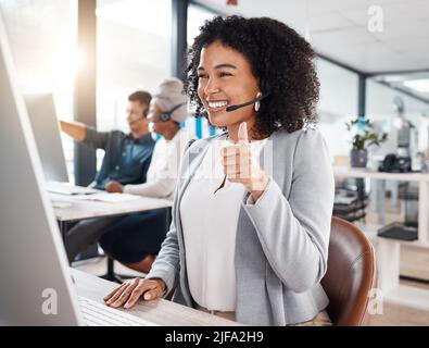 Felice agente di telemarketing del call center di gara mista gesturing thumbs in su durante la riunione virtuale via videochiamata su un computer in un ufficio. Femmina Foto Stock