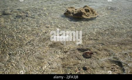 La coppa trasparente di plastica viene trasportata dal vento al mare nella zona costiera. Inquinamento plastico della zona surf. Mar Rosso, Egitto Foto Stock