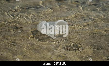 La coppa trasparente di plastica viene trasportata dal vento al mare nella zona costiera. Inquinamento plastico della zona surf. Mar Rosso, Egitto Foto Stock