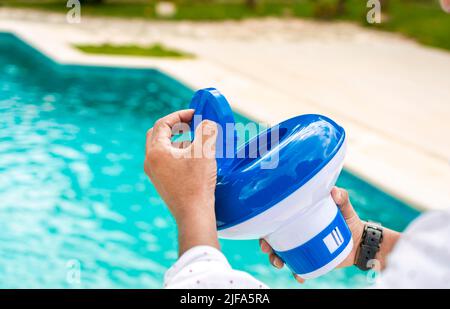 Mani di un lavoratore che installa un galleggiante di cloro di piscina, una persona che tiene un distributore di cloro di piscina. Mani che tengono un distributore di cloro per piscine. Mano di un Foto Stock