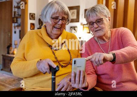 Due anziani, sorelle, che guardano uno smartphone in casa, Bocholt, Renania settentrionale-Vestfalia, Germania Foto Stock