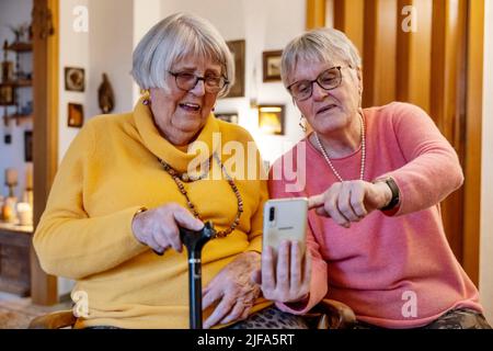 Due anziani, sorelle, che guardano uno smartphone in casa, Bocholt, Renania settentrionale-Vestfalia, Germania Foto Stock