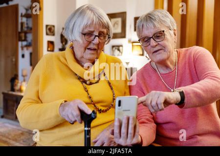 Due anziani, sorelle, che guardano uno smartphone in casa, Bocholt, Renania settentrionale-Vestfalia, Germania Foto Stock