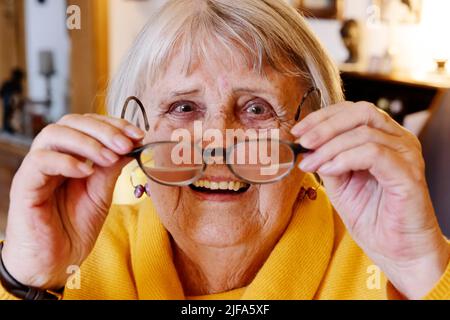 Donna anziana indossa i suoi occhiali sorridenti a casa, Bocholt, Renania settentrionale-Vestfalia, Germania Foto Stock