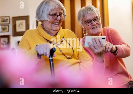 Due anziani, sorelle, che guardano uno smartphone in casa, Bocholt, Renania settentrionale-Vestfalia, Germania Foto Stock