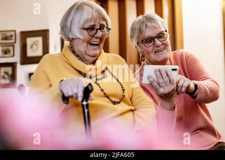 Due anziani, sorelle, che guardano uno smartphone in casa, Bocholt, Renania settentrionale-Vestfalia, Germania Foto Stock