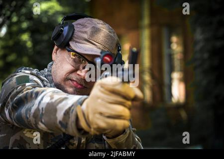 Giovane uomo alla polizia civile corso tattico. Uomo con una pistola in uniforme militare cuffie protettive tattiche. Addestramento della polizia nella galleria di tiro con l'arma. Messa a fuoco selettiva a portata di mano. Foto Stock