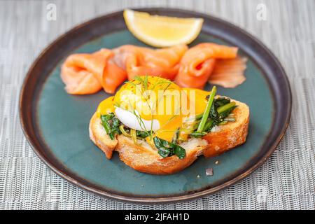 Uova fresche Benedetto con salmone affumicato e fetta di limone su piatto nel ristorante. Cibo gourmet dell'hotel con pane tostato al forno e uova in camicia, sano Foto Stock