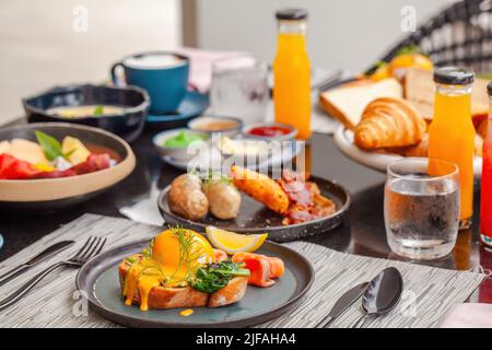 Deliziosa colazione in hotel di lusso. Tavolo con piatti pieni di vari cibi freschi in caffetteria, spremute fresche, uova, frutta e salsicce. Mattina Foto Stock