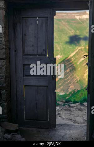 Porta di legno nelle rovine di una casa abbandonata attraverso la quale sono visibili le montagne, nelle rovine del villaggio fantasma di Gamsutl in Dagestan Foto Stock