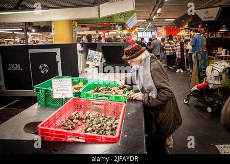 Foto di una vecchia donna nel mercato marchigiano des Capucins a Bordeaux, alla ricerca di ostriche e conchiglie di pesce, in vendita su una stalla. Ostriche sono Foto Stock