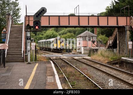 Stazione di Crediton, incrocio di livello e scatola del segnale, Crediton, Devon. Il segnalatore riceve il gettone dal macchinista del treno dalla sezione di Okehampton. Foto Stock