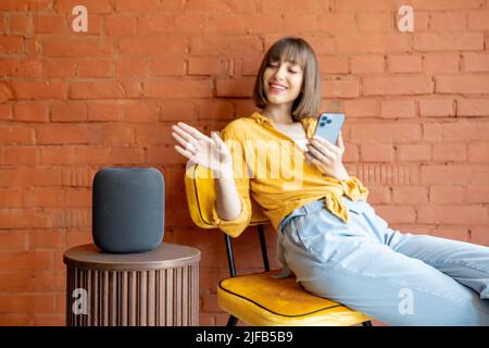 Donna con altoparlante intelligente e telefono a casa Foto Stock