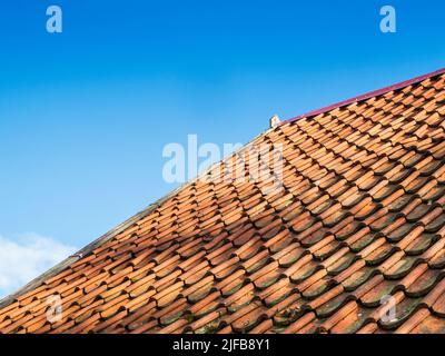 Vista parziale laterale obliqua di un tetto a falde coperto da scandole nella vista dal basso di fronte a un cielo senza nuvole al sole. Foto Stock