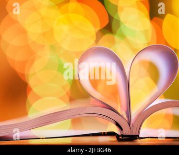 Apri il libro con il segno del cuore fatto da pagine su uno sfondo sfocato con copyspace e bokeh. L'istruzione è motivante e promuove l'innovazione. Amore Foto Stock