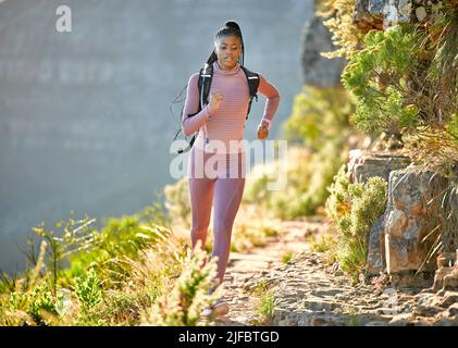 Giovane fit e attiva donna afroamericana escursioni e jogging attraverso le montagne in una giornata estiva soleggiata. Donna nera che corre da sola esercitandosi e. Foto Stock