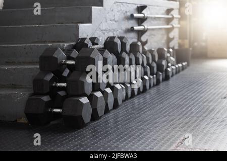 Primo piano di un gruppo di pesi palestra sul pavimento in un club vuoto di salute e sport. Vista macro dei pesi dei manubri in una sala esercizi buia Foto Stock