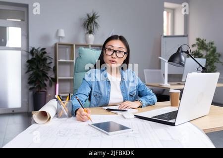 Ritratto di giovane donna designer in ufficio moderno al lavoro, donna asiatica di successo in occhiali guardando la macchina fotografica. Foto Stock