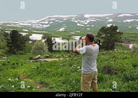 l'uomo ama la natura e guarda attraverso il binocolo. Un uomo turistico guarda attraverso binocoli nelle montagne dell'altopiano di Lagonaki Foto Stock