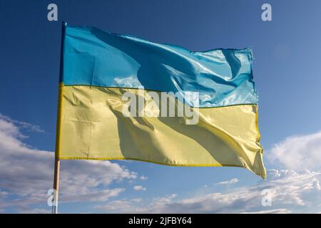 La bandiera dell'Ucraina indipendente soffia nel vento contro il cielo blu e il sole che tramonta Foto Stock