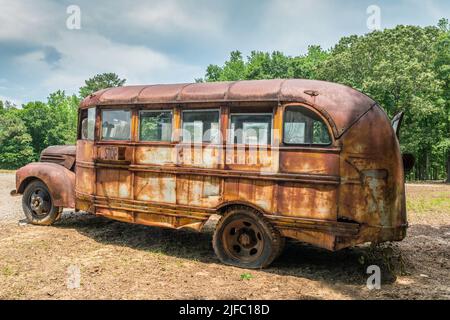 Vecchio arrugginito abbandonato scuolabus dal 1940 's parcheggiato in un campo con un pneumatico piatto e finestre rotte profilo closeup Foto Stock