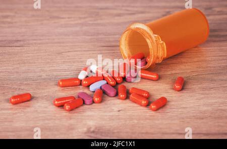 Una bottiglia arancione aperta di pillole dai colori vivaci versate su un tavolo di legno. I supplementi della vitamina sono un buon senso rimanere sani. Cronico e. Foto Stock