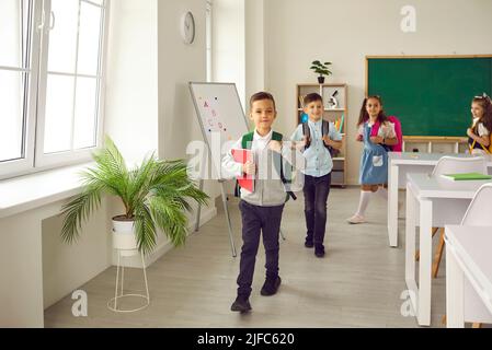 Gruppo di ragazzi delle scuole elementari felici che lasciano l'aula alla fine della lezione Foto Stock