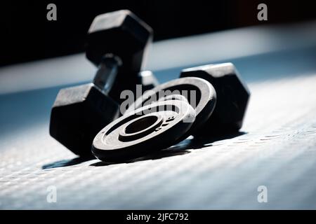 Primo piano di un gruppo di pesi palestra sul pavimento in un club vuoto di salute e sport. Vista macro dei pesi dei manubri in una sala esercizi buia Foto Stock