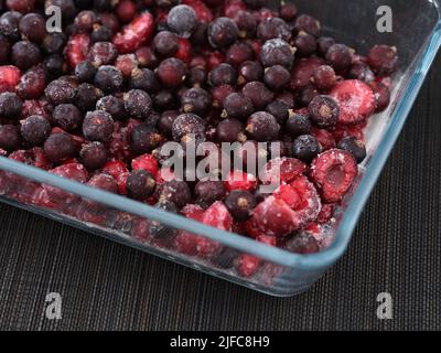 Ribes nero e rosso surgelati con ciliegie in un contenitore di vetro. Primo piano. Tasto basso. Foto Stock