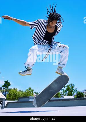 Giovane, giovane ed elegante ragazzo afroamericano che esegue trucchi per skate sulla sua tavola al parco skate. Un giovane uomo concentrato che si esibisce sul suo skateboard Foto Stock