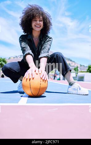 Allegra giovane africana donna con ricci afrofroche squadrano e tengono una pallacanestro in campo. Ritratto di donna sorridente che sta per giocare un gioco Foto Stock