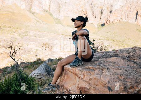 Donna sorridente escursionista seduto su grande pietra in valle godendo la vista Foto Stock