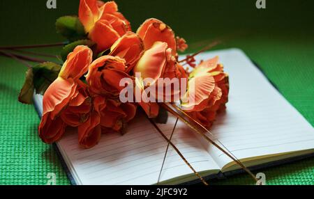 Sopra il colpo dei fiori arancioni su un blocco note aperto. La natura può ispirarci a scrivere e a stimolare la nostra creatività. Produttività e motivazione in un ambiente creativo Foto Stock