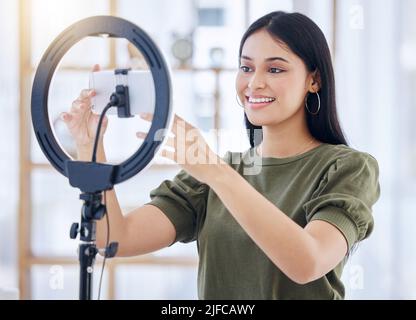 Millennial beauty blogger sorridendo mentre si regola il suo smartphone sulla ghiera o premendo record . Bella giovane influencer utilizzando una luce ad anello Foto Stock