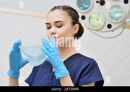 bella giovane donna in un vestito chirurgico mette su una maschera sterile. Foto Stock